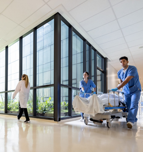 Krankenpfleger transportieren einen Patienten auf einer Trage durch ein Krankenhaus – Krankenhausüberweisungen von Vestische Fahrdienste